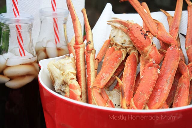 Grilled crab legs in a red bowl next to bottles of soda and straws