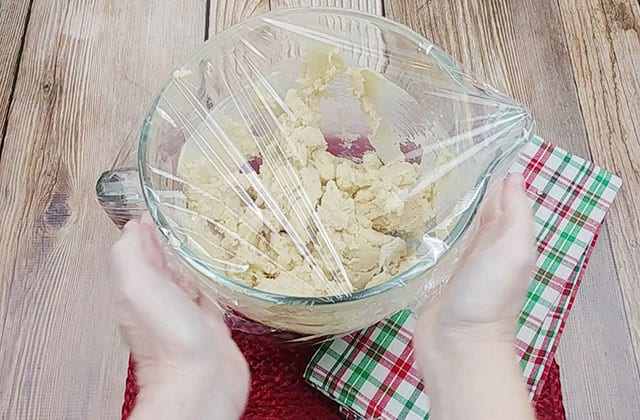 Covering a glass bowl with plastic wrap filled with cookie dough
