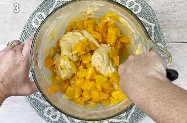 Stirring peaches into the bread batter in a glass mixing bowl