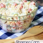 Shoepeg corn salad in a clear glass bowl with a wooden spoon