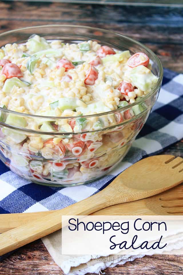 Shoepeg corn salad in a clear glass bowl with a wooden spoon
