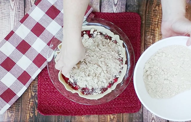 Sprinkling crumb topping over cherry pie filling in dish