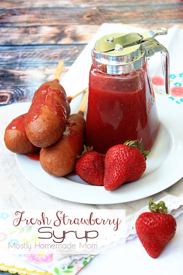 Strawberry syrup in a glass container on a plate with strawberries and pancakes