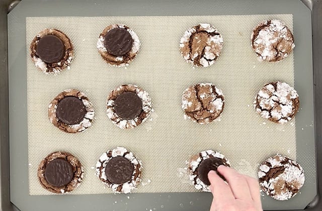 Putting a peppermint patty in the center of cookies on a cookie sheet