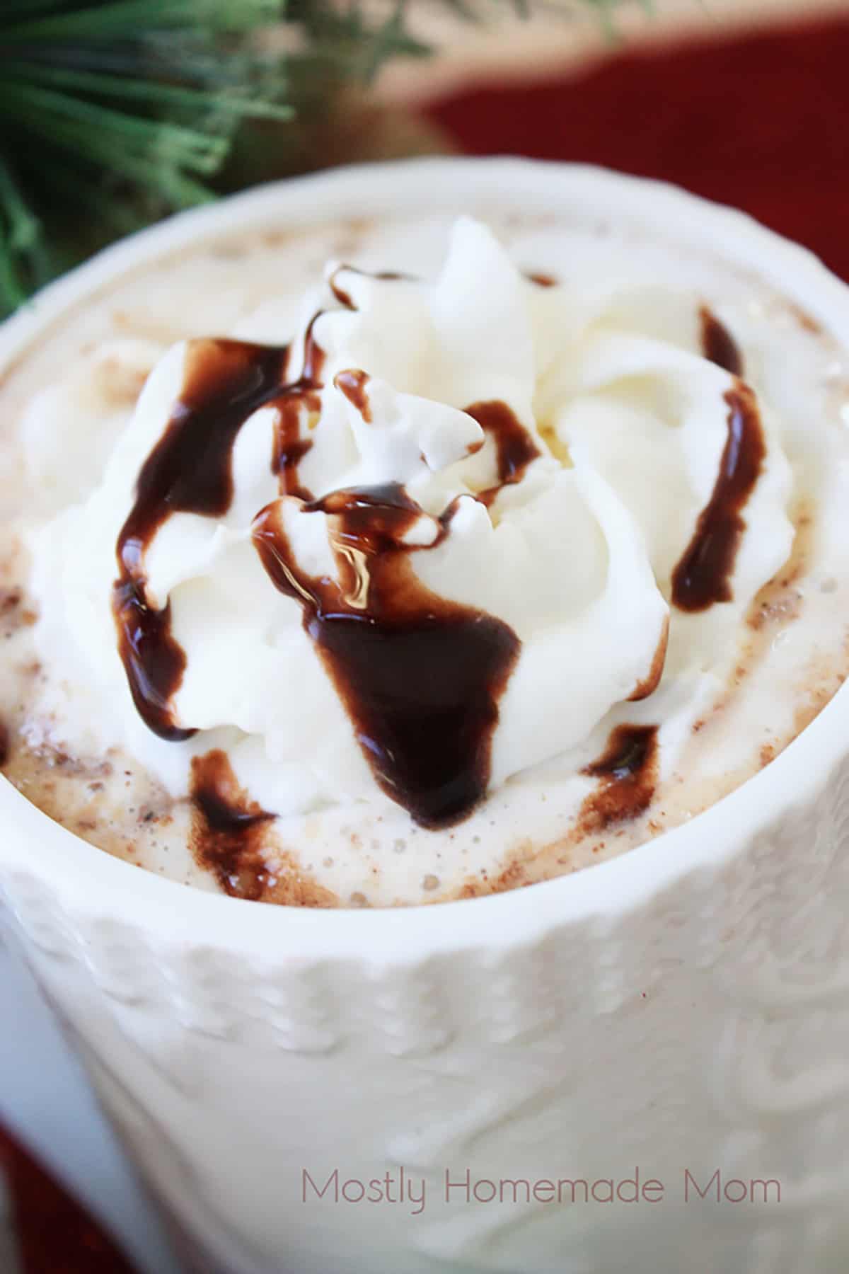Whipped cream and chocolate syrup on top of eggnog hot chocolate.