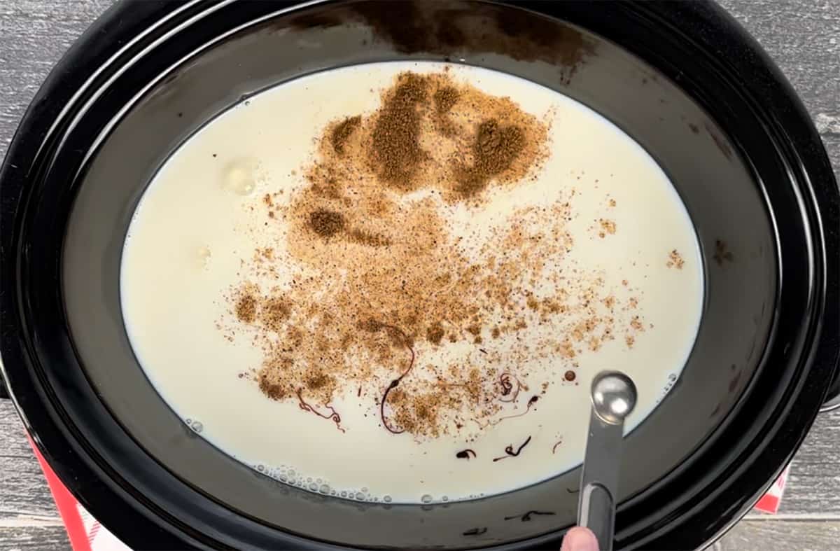 Sprinkling ground nutmeg into a mixture in a slow cooker.