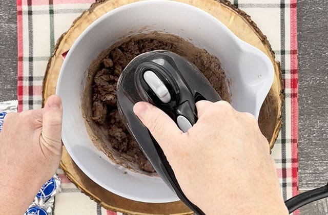 Mixing the cookie dough in a white mixing bowl with a black hand mixer