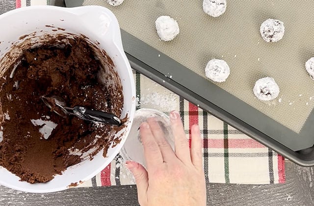 Rolling cookie dough in powdered sugar and placing them on a cookie sheet