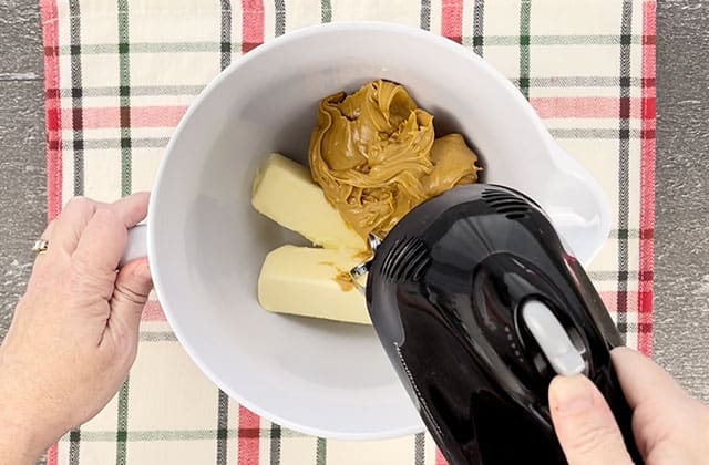 Blending butter and peanut butter in a white mixing bowl with a hand mixer