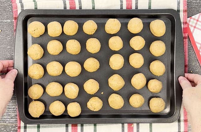 Lifting a cookie sheet filled with uncoated bon bons to the refrigerator