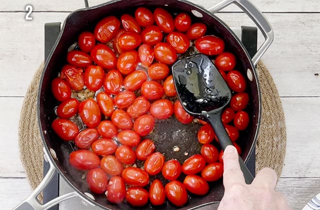 Cooking cherry tomatoes in a skillet on the stove with a black spatula