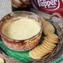 Clam dip in a baking dish with crackers and soda in the background