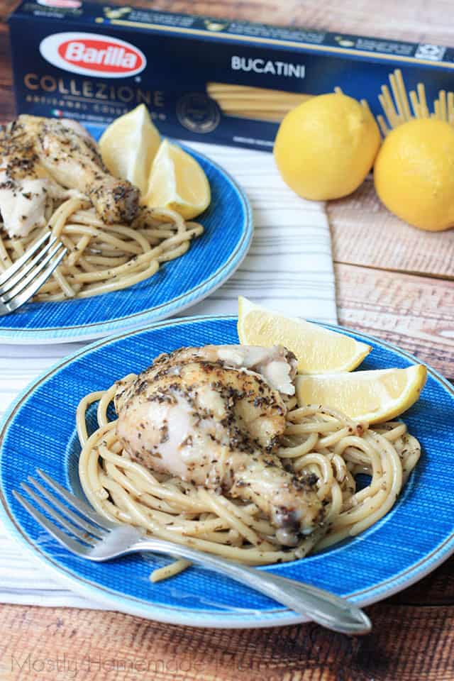 Two plates of greek lemon chicken with lemon slices over pasta