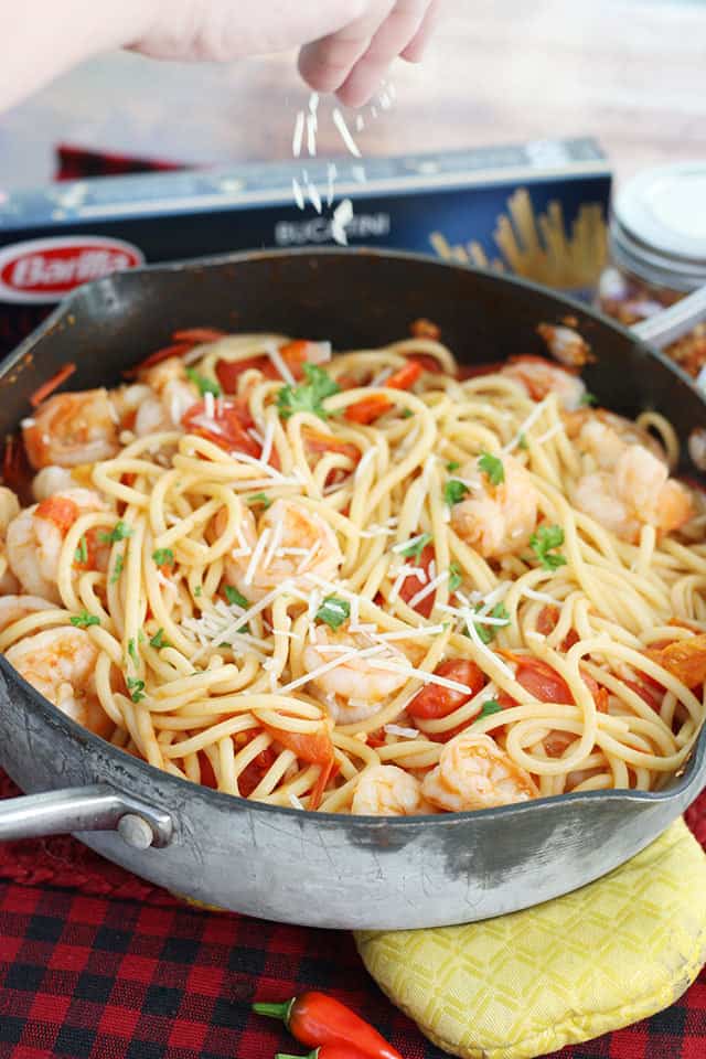spicy shrimp pasta in a skillet with Parmesan cheese being sprinkled