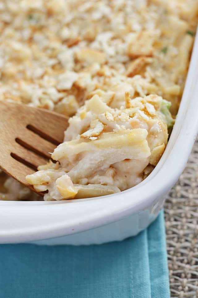 A wooden spoon scooping out cheesy shrimp casserole from a dish