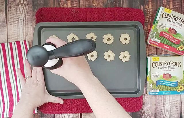 Using a cookie press to press out cookie dough onto a cookie sheet