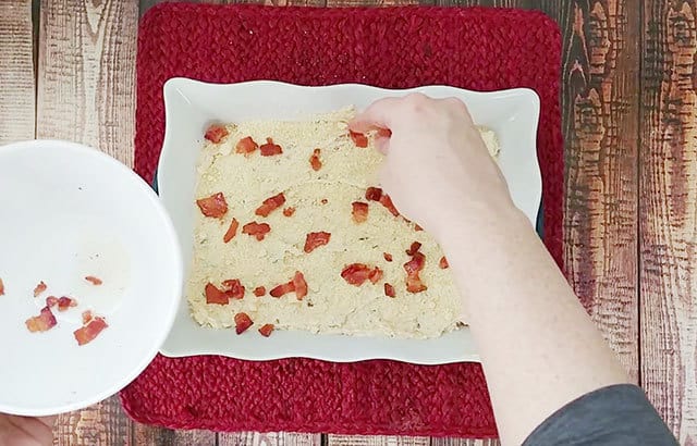 Sprinkling bacon pieces over jalapeno popper dip