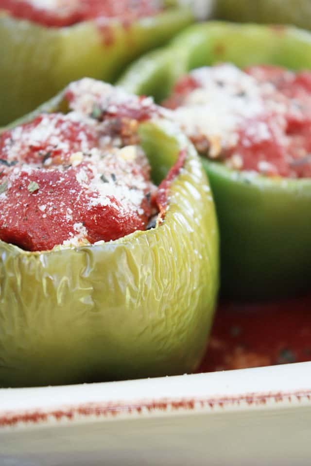 A stuffed green pepper topped with parmesan cheese in a baking dish