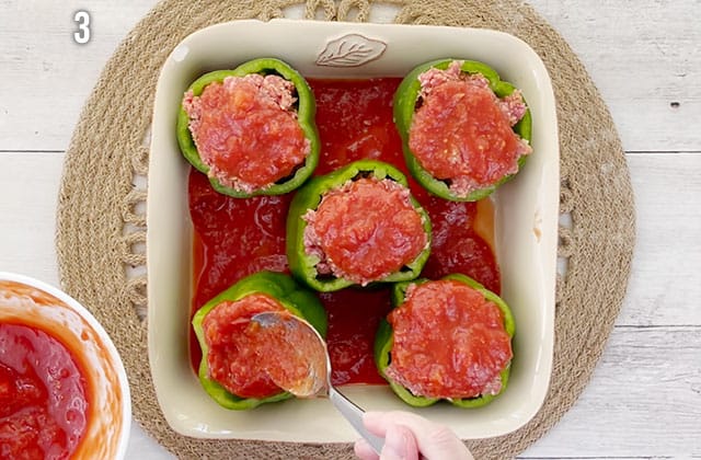 Spreading crushed tomatoes over stuffed peppers in a baking dish