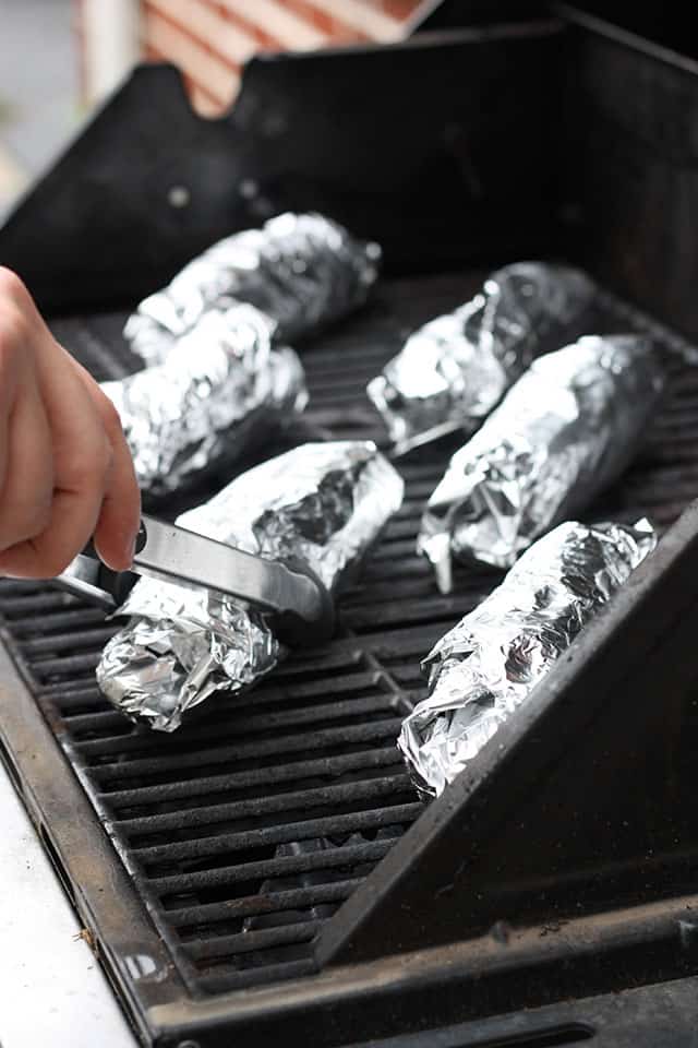 Foil wrapped ears of corn on a grill outside