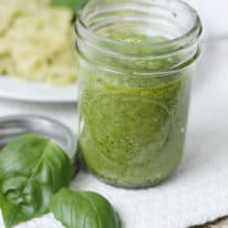 Spinach pesto in a mason jar next to fresh basil leaves