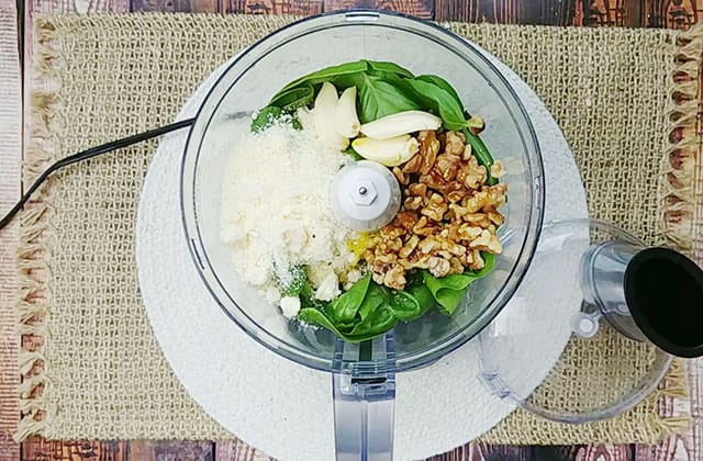 Spinach, basil, garlic, and walnuts in a food processor bowl
