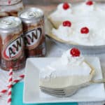 A slice of root beer float pie on a white plate with cans of root beer in the background