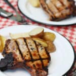 Grilled bone in pork chops on white plates with roasted potatoes