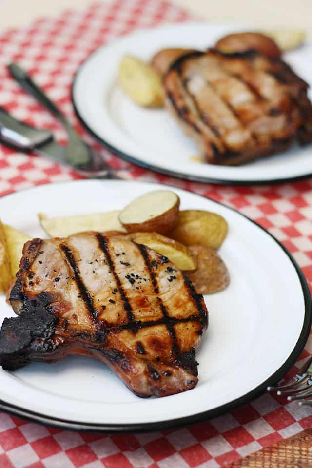 Grilled bone in pork chops on white plates with roasted potatoes