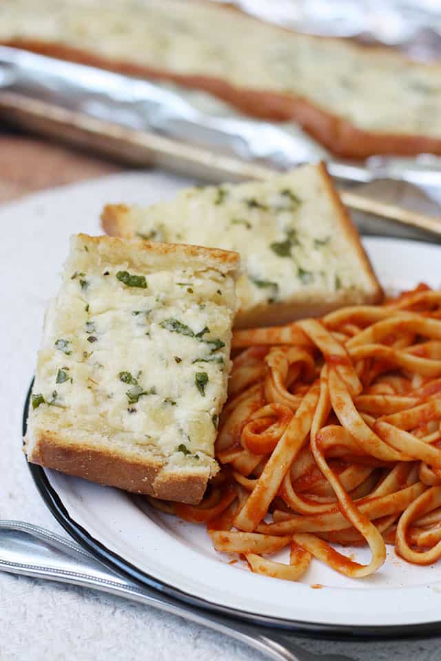 Two slices of homemade garlic bread on a white plate next to pasta