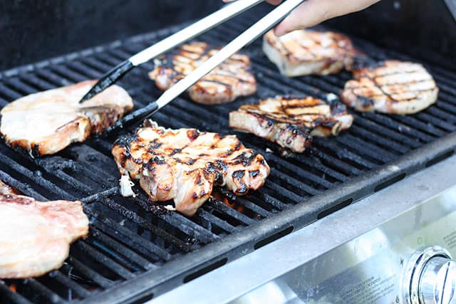 Using tongs to flip pork chops on a gas grill