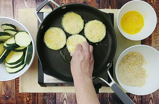 Frying breaded zucchini slices in a skillet with olive oil
