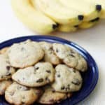 Banana chocolate chip cookies on a blue plate with bananas in the background