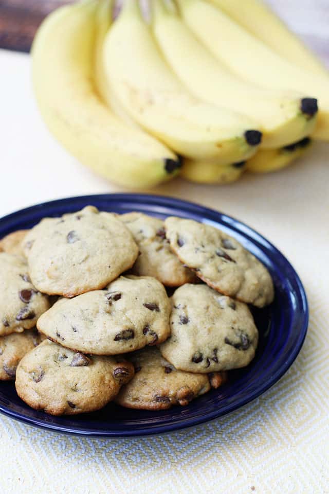 Banana chocolate chip cookies on a blue plate with bananas in the background