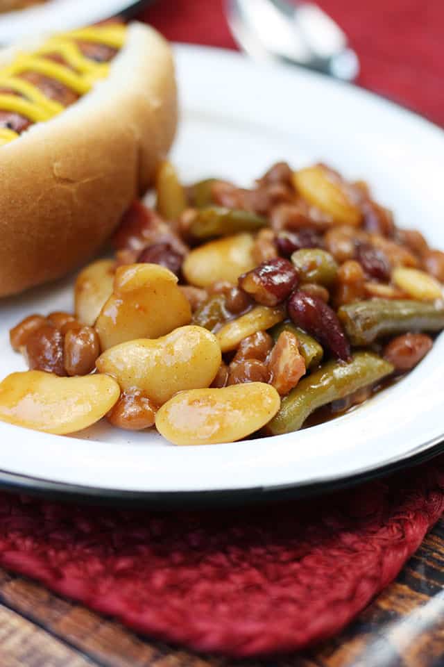 Baked beans on a white plate next to a hot dog with mustard