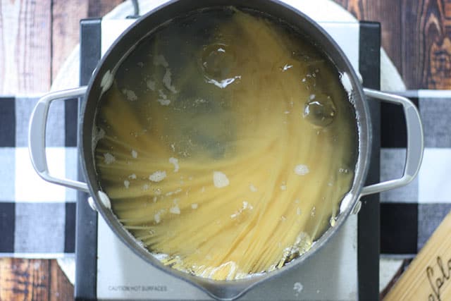 Bucatini pasta in boiling water in a large pot on the stove