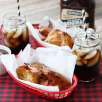 Two baskets with wax paper filled with honey glazed chicken wings next to glasses of soda