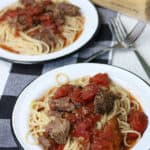 Slow cooker braised beef over bucatini pasta on two small white plates