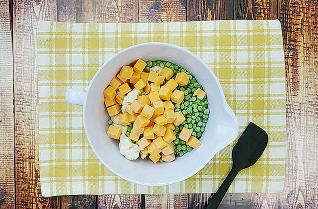 Cauliflower, peas, and cheese in a white mixing bowl