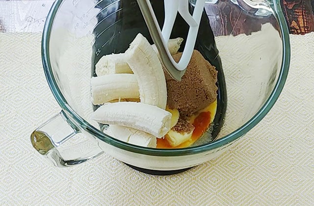 Butter, eggs, brown sugar, and bananas in a glass bowl of a stand mixer