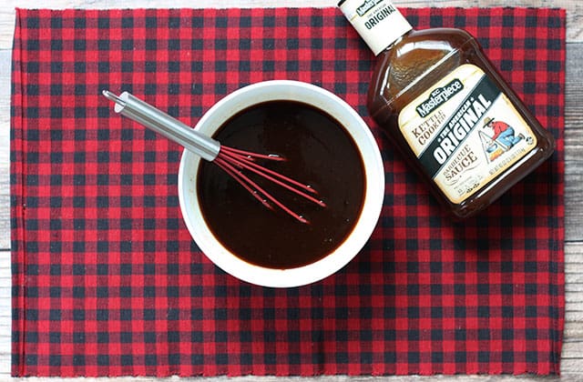 Honey bbq glaze in a white bowl with a whisk next to a bottle of bbq sauce