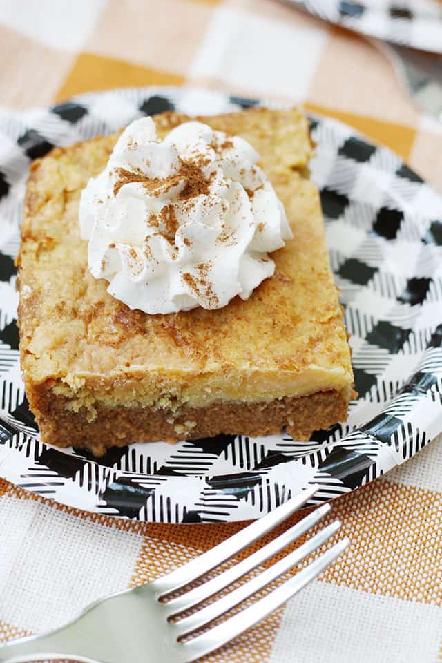 A close up picture of a slice of pumpkin dump cake topped with whipped cream and pumpkin pie spice
