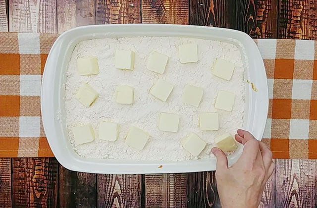 Laying slices of butter on top of pumpkin dump cake in a white baking dish before baking