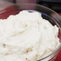 A bowl of crockpot mashed potatoes sitting in front of a stainless steel crockpot