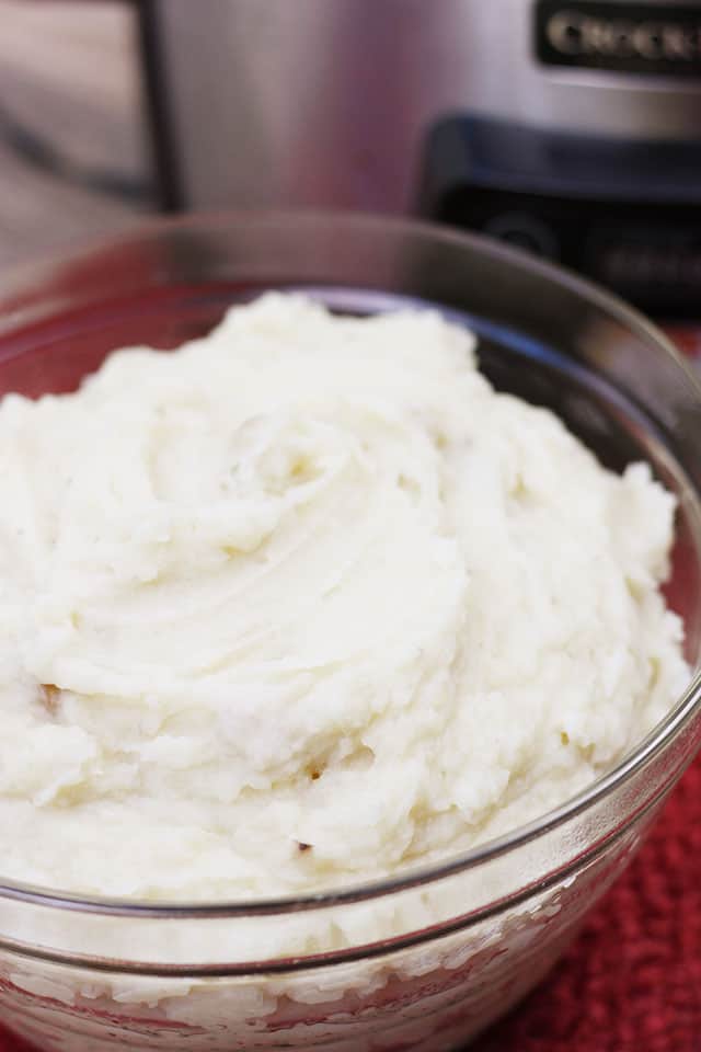 A bowl of crockpot mashed potatoes sitting in front of a stainless steel crockpot