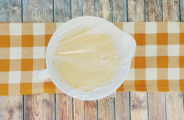 Pumpkin dip in a white mixing bowl covered with plastic wrap