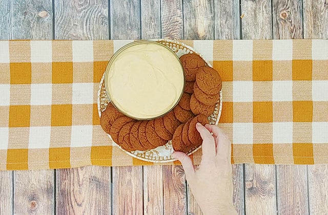 Placing ginger snap cookies on a plate next to a bowl of pumpkin dip