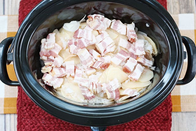 Sliced potatoes, onion, and bacon in a black slow cooker