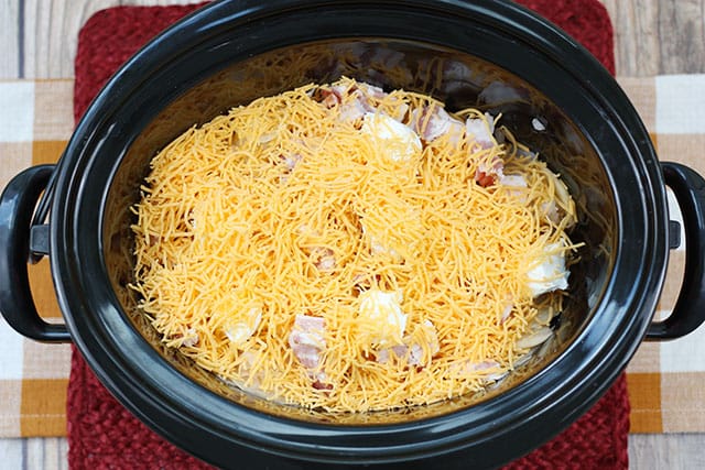 Shredded cheese on top of the ingredients in the slow cooker