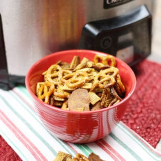 Crockpot Chex Mix in a red bowl in front of a stainless steel crockpot